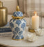 Decorative ceramic jar with blue floral patterns on a marble surface with candles and books in the background.