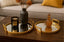 Decorative setup with two mirrored gold trays, a candle, and a vase on a wooden surface.