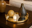 Decorative vases and a candle on a mirror gold round tray on a wooden surface.