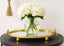 Gold mirrored tray with a vase of white flowers on a black surface