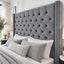 A large grey tufted velvet headboard with silver nailhead trim on a bed in a styled bedroom setting.