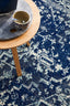 Detailed view of the Evoke 253 Navy Rug with a side table and coffee cup.