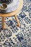 Close-up of ivory rug featuring bold navy motifs placed under round wooden side table.