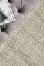 Soft textured rug in silver tones placed near tufted sofa, showcasing detailed woven floral patterns.