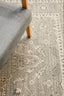 Close view of silver rug corner with intricate design placed under a modern wooden chair.