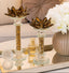 Decorative candle holders on a mirror surface with flowers and perfume bottle in the background