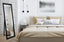 Black French provincial free standing mirror styled in bedroom with beige bedding and wall art.