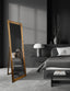 Gold French provincial free standing mirror styled in dark bedroom with grey bed and lamp.