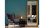 Gold French provincial ornate mirror styled beside teal wall, armchair and cozy bedroom corner.