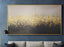 Abstract art piece with gold and black gradient on a blue wall above a gray sofa.