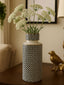 Decorative vase with patterned design containing white flowers on a wooden surface.