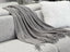  Cozy Levi Throw Rug Blanket in dark grey draped over a sofa, adding a touch of elegance with its fringe edges.