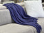 Stylish Levi Throw Rug Blanket in blue draped over a sofa, adding rich color and texture.