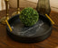 Decorative black textured marble tray with gold handles holding a green decorative ball on a wooden surface.