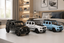 Three Mercedes-Benz G-Class model cars in black, white, and light blue are displayed on a white table in a modern bedroom setting.