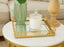 Gold mirror rectangle tray with a green vase and glass jar on a marble table