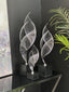 Elegant silver Ribbon Table Décor set in small, medium, and large sizes displayed on a black console against a dark backdrop with greenery – showcasing a modern and artistic interior accent.