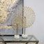 Stylish gold flower stem décor set on marble base, displayed on a glass table with elegant wall art in the background.