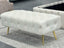 Beige Shirley Ottoman with gold legs, tufted velvet design, styled in modern living room.
