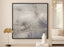 Abstract art piece with a hint of silver with black border on a wall in a living room setting with decor elements.