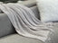 Grey Tessa throw rug blanket laid over a blue sofa, featuring a detailed textured weave and fringe ends.